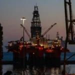 Offshore oil rig silhouette at sunset with a red downward trend arrow breaking an oil barrel for UAE OPEC exit analysis